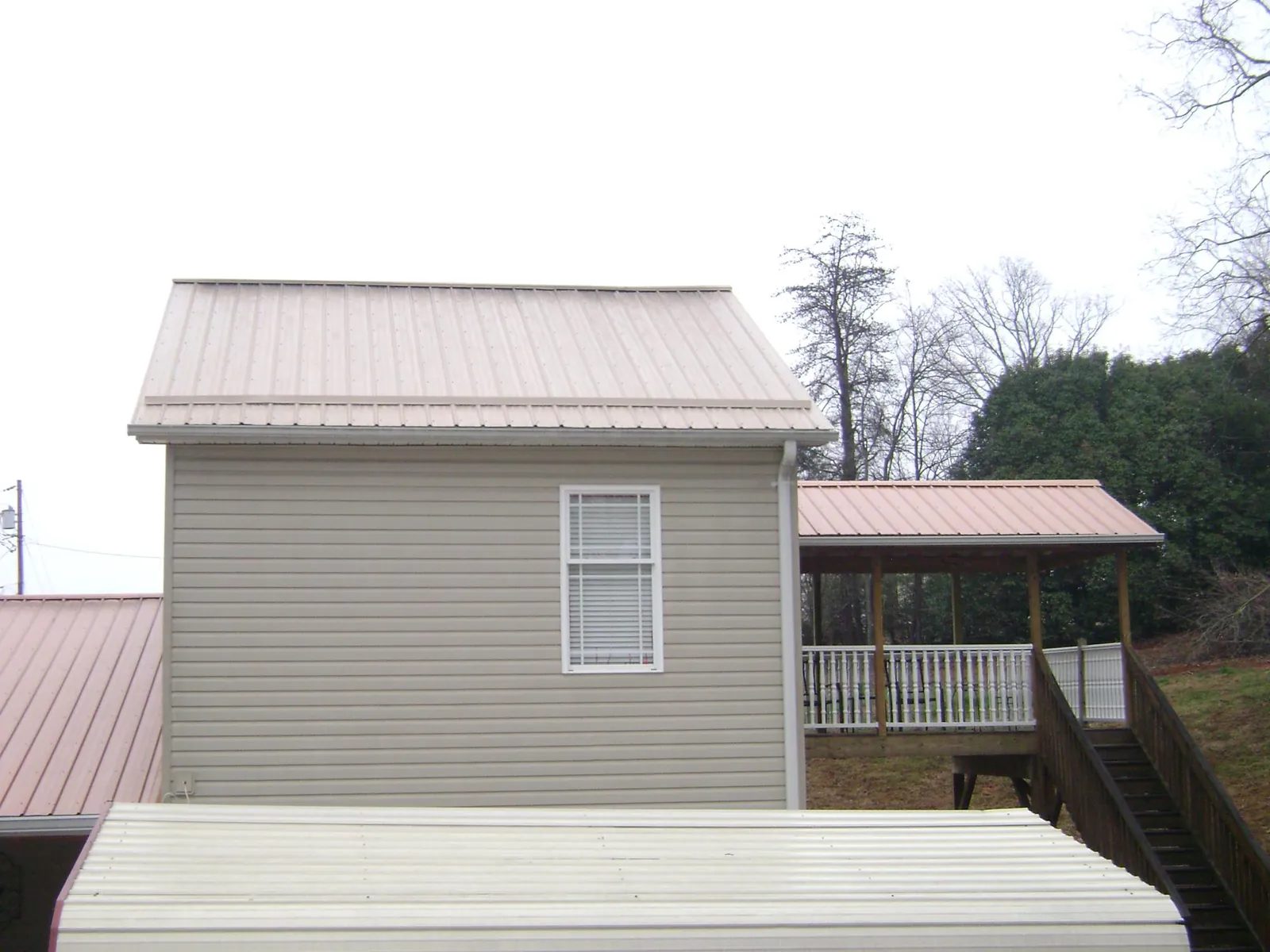 Tan metal roofs on a two story addition and attached porch, from a Roof Replacement job in Fairview